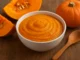 Pumpkin puree in a bowl with slices of pumpkin and spoon on a wooden table